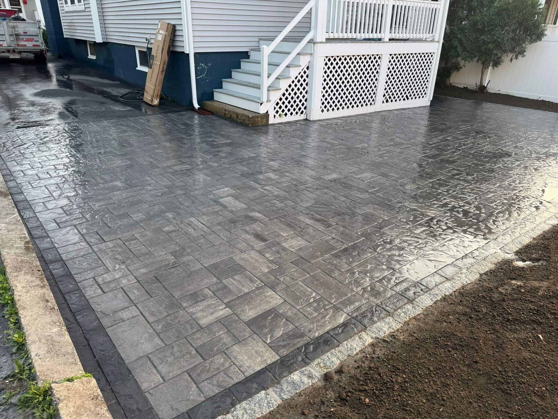 Wet gray paver driveway beside a blue house with white railings and a small ramp.