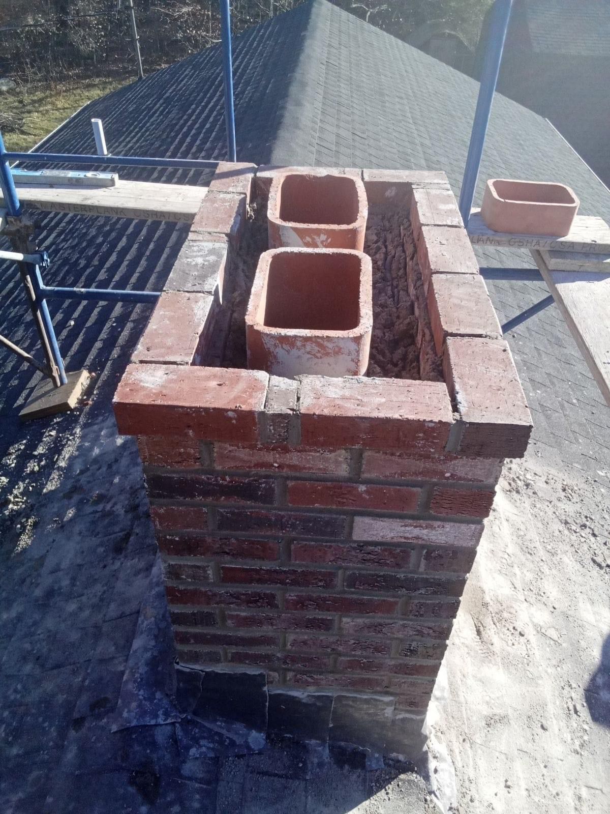 Brick chimney under construction with two cinder block flues on a rooftop or patio.