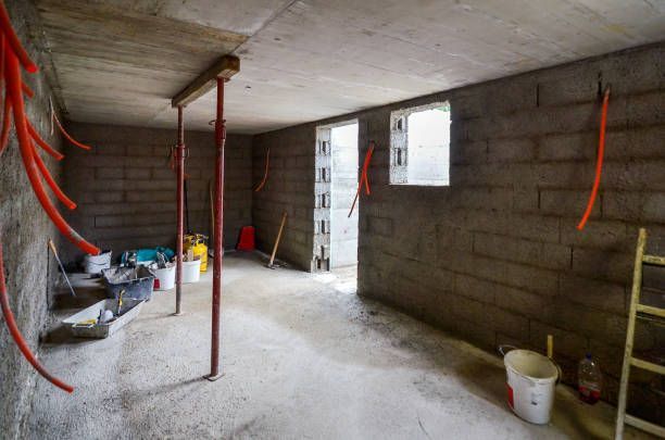 Unfinished basement under construction with cinder block walls, exposed wiring, and construction tools.