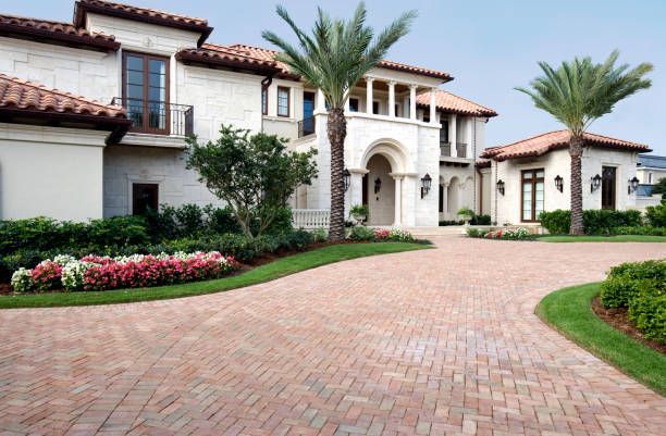 Large Mediterranean-style mansion with a brick driveway, palm trees, and landscaped gardens