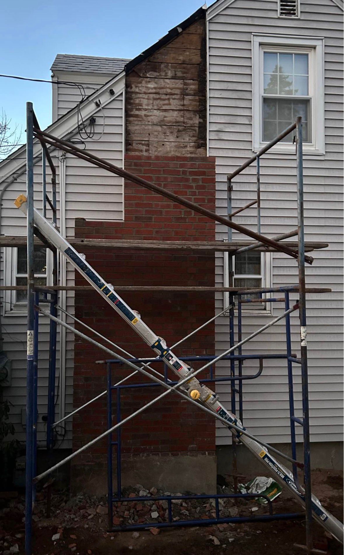 Scaffolding against a weathered brick wall beside two gray-sided buildings during exterior repairs