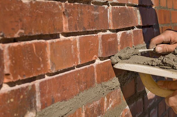 Brick wall being pointed with mortar by a worker using a trowel.