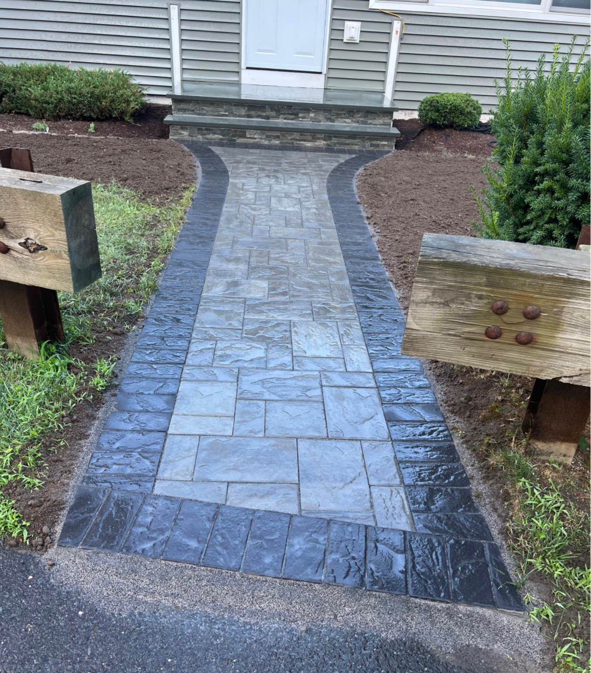 Stone walkway leads to a house front door, bordered by dark gravel and landscaped shrubs.