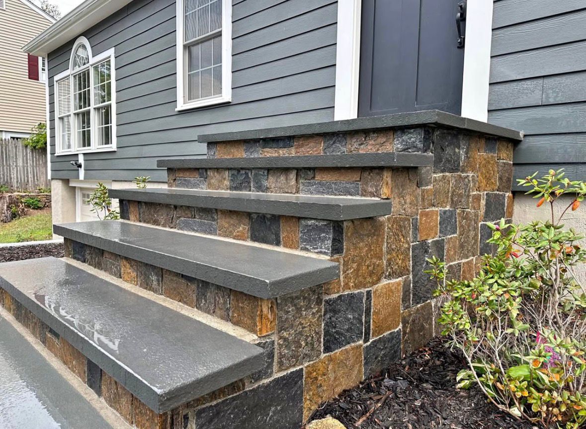 Stone and gray wooden front steps leading to a house entrance with siding and windows