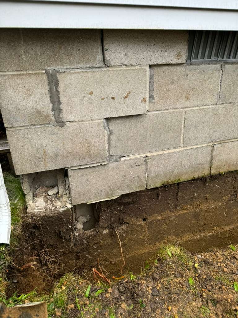Cracked cinder block foundation with moisture stains and moss near the ground.