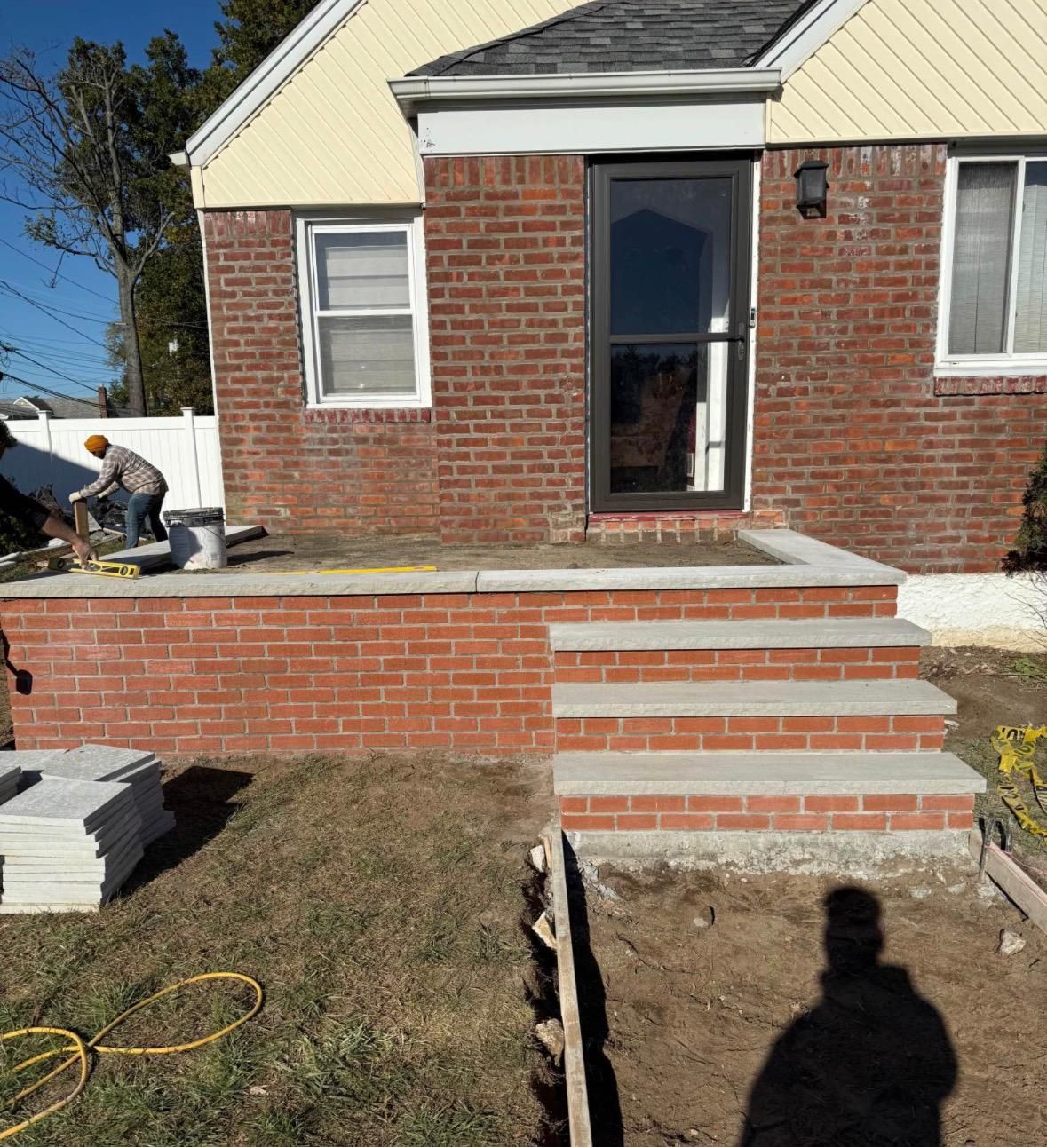 Brick house with a front porch and steps under construction in a yard.