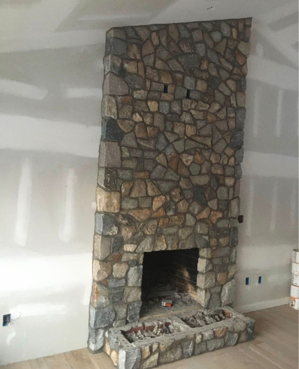 Stone fireplace with a rough rock facade in an unfinished room with white walls.