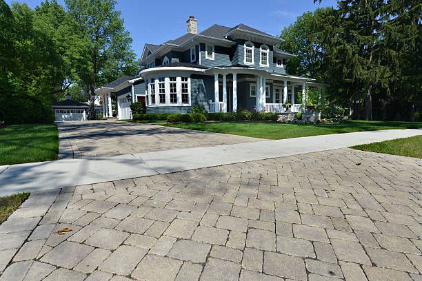 Large gray house with white trim and a stone driveway surrounded by trees and lawn
