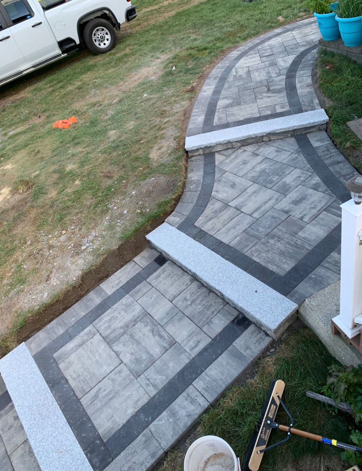 Curved gray paver walkway with a ramp, leading past a lawn and parked white truck.
