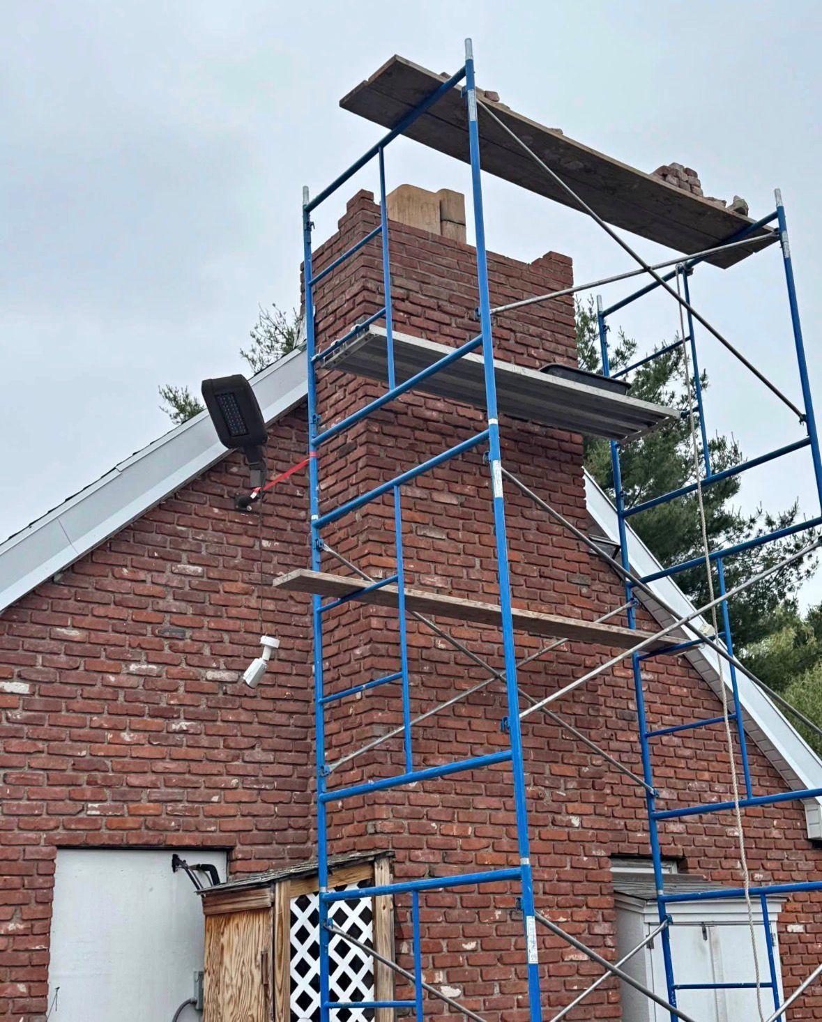 Blue scaffolding beside a brick house with a chimney under repair