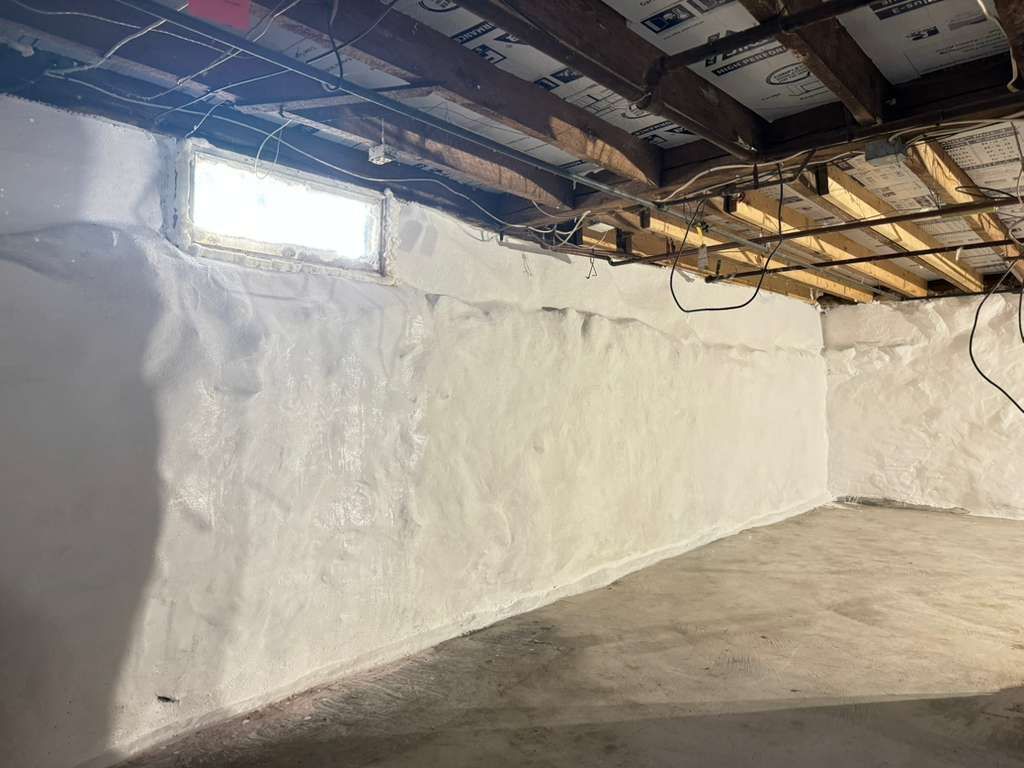Empty basement with white-painted walls, exposed ceiling beams, and a small window.