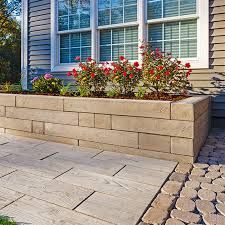 Raised stone planter with red and pink flowers beside a tiled walkway and house windows