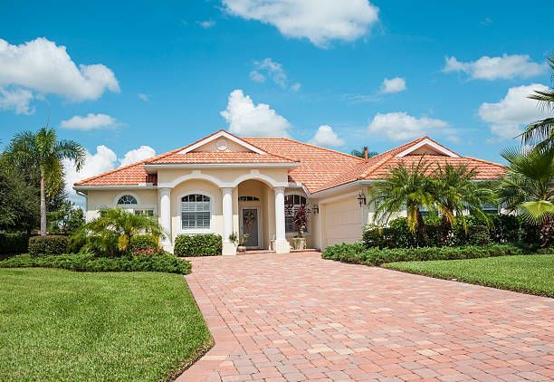 Single-story house with red tile roof, arched entrance, and brick driveway under a blue sky