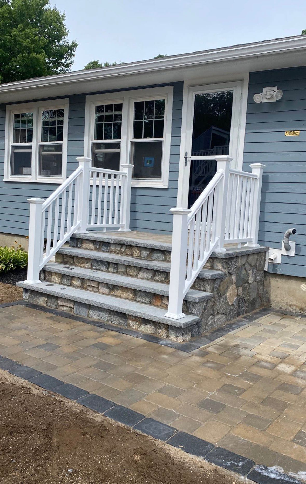 Front entrance of a blue house with stone steps, white railings, and a paved walkway.