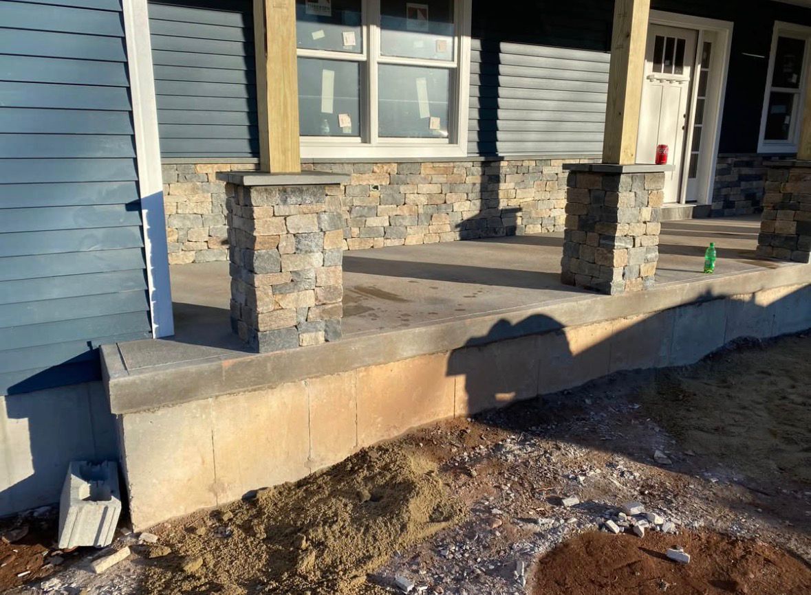 Stone-front porch and steps on a house exterior with blue siding and a concrete retaining wall.