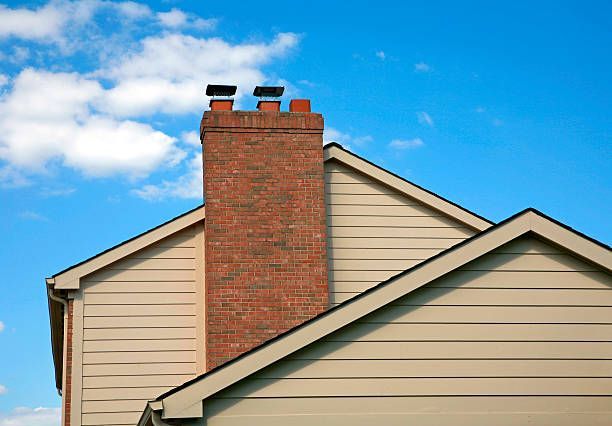 Red brick chimney above beige house roof against a blue sky with clouds
