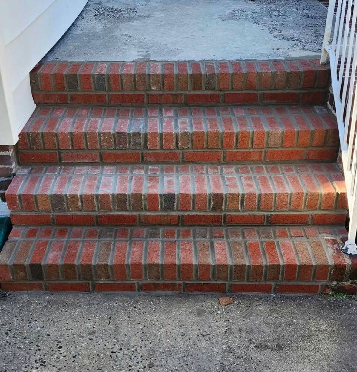Red brick front steps leading to a concrete landing, with white railings on both sides.
