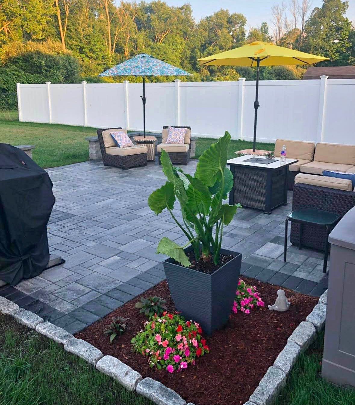 Backyard patio with potted plant and flowers, wicker seating, grill, and white privacy fence at sunset