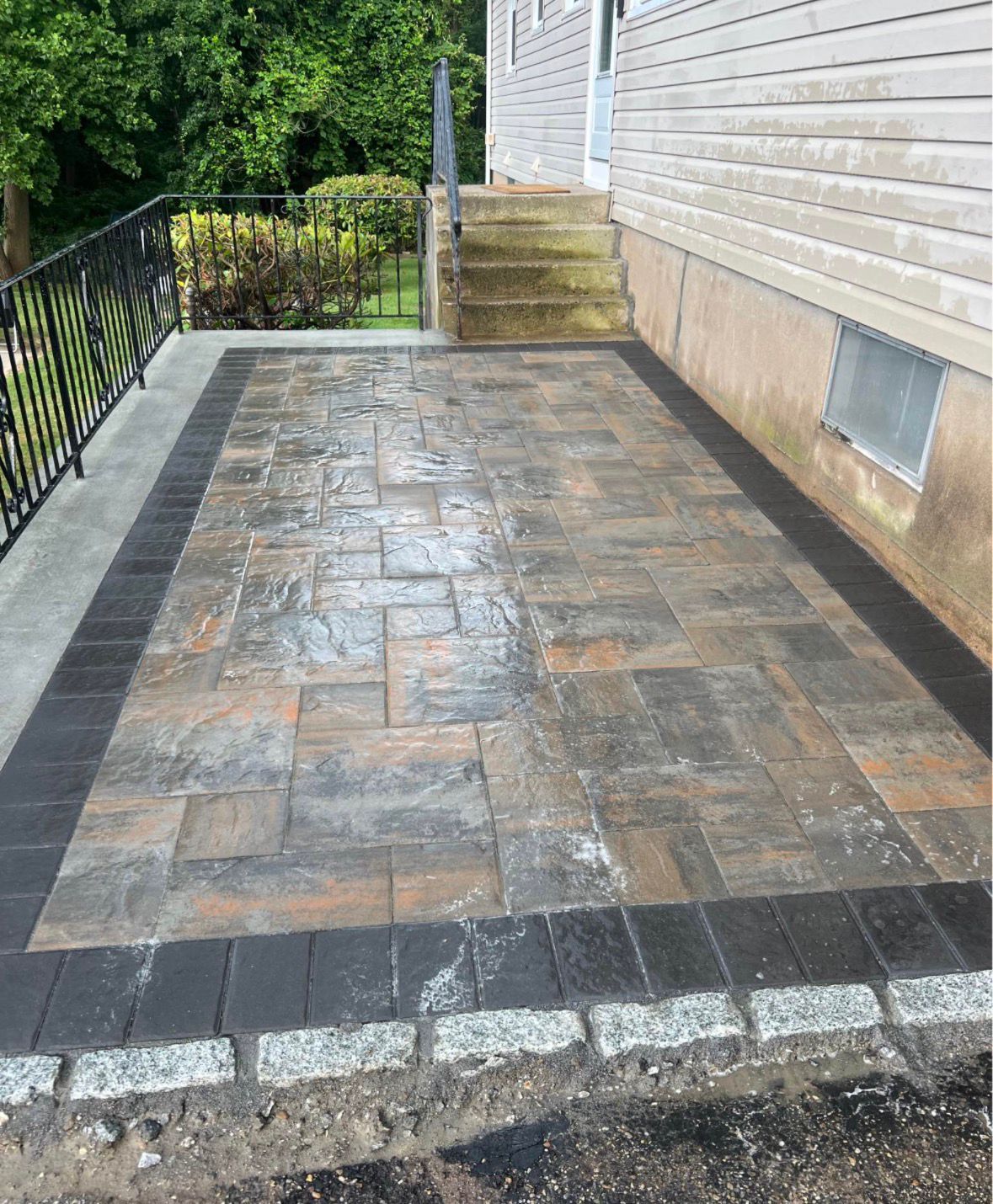 Paved patio beside a house with wet stone pavers, a black border, and steps leading up to a door