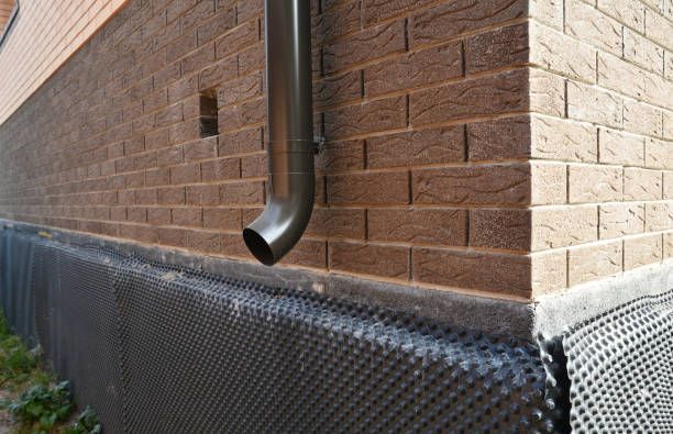 Brick building wall with a downspout and black gravel barrier at the foundation