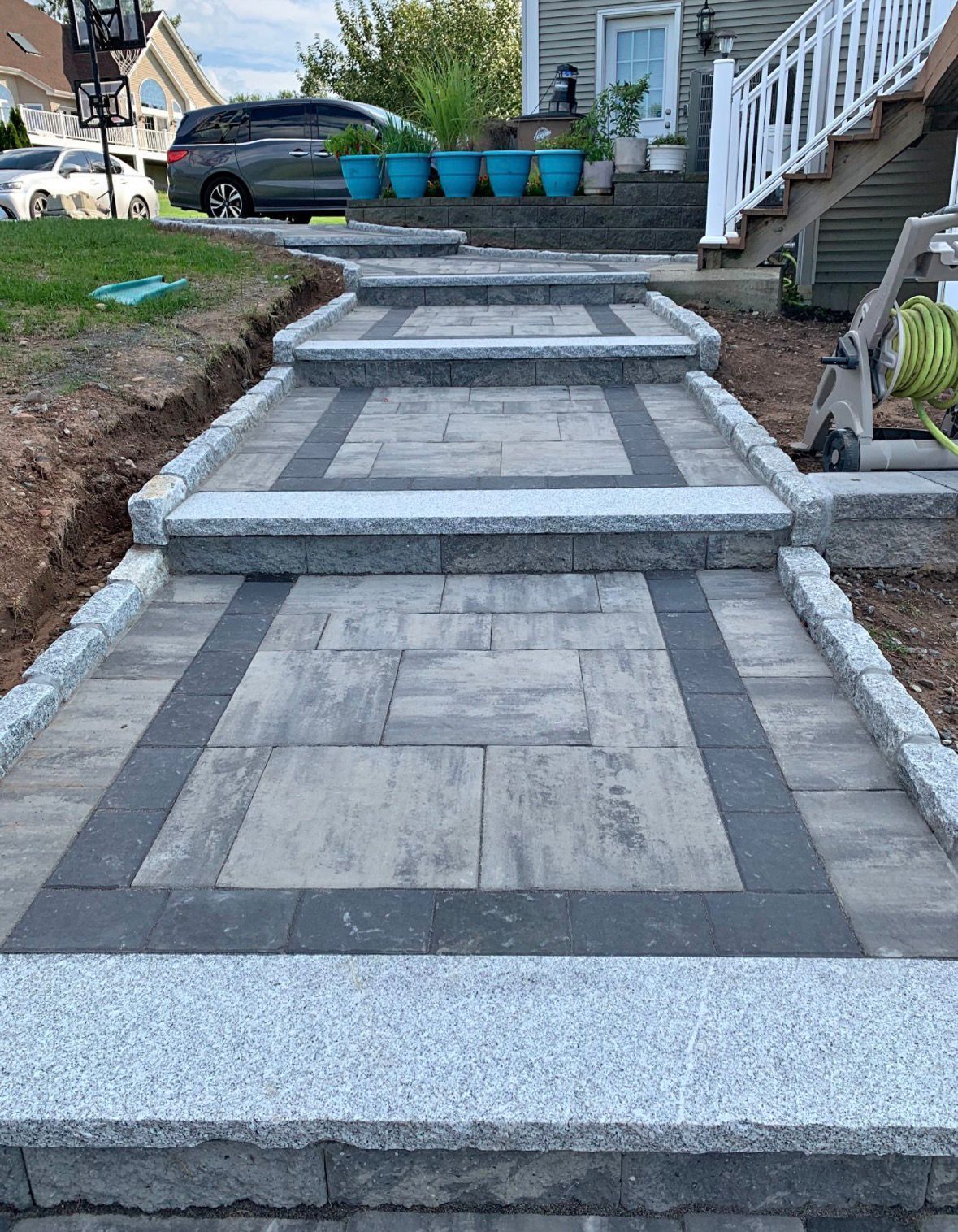 Front walkway with stone pavers and gray borders leading up a house with steps and blue planters.