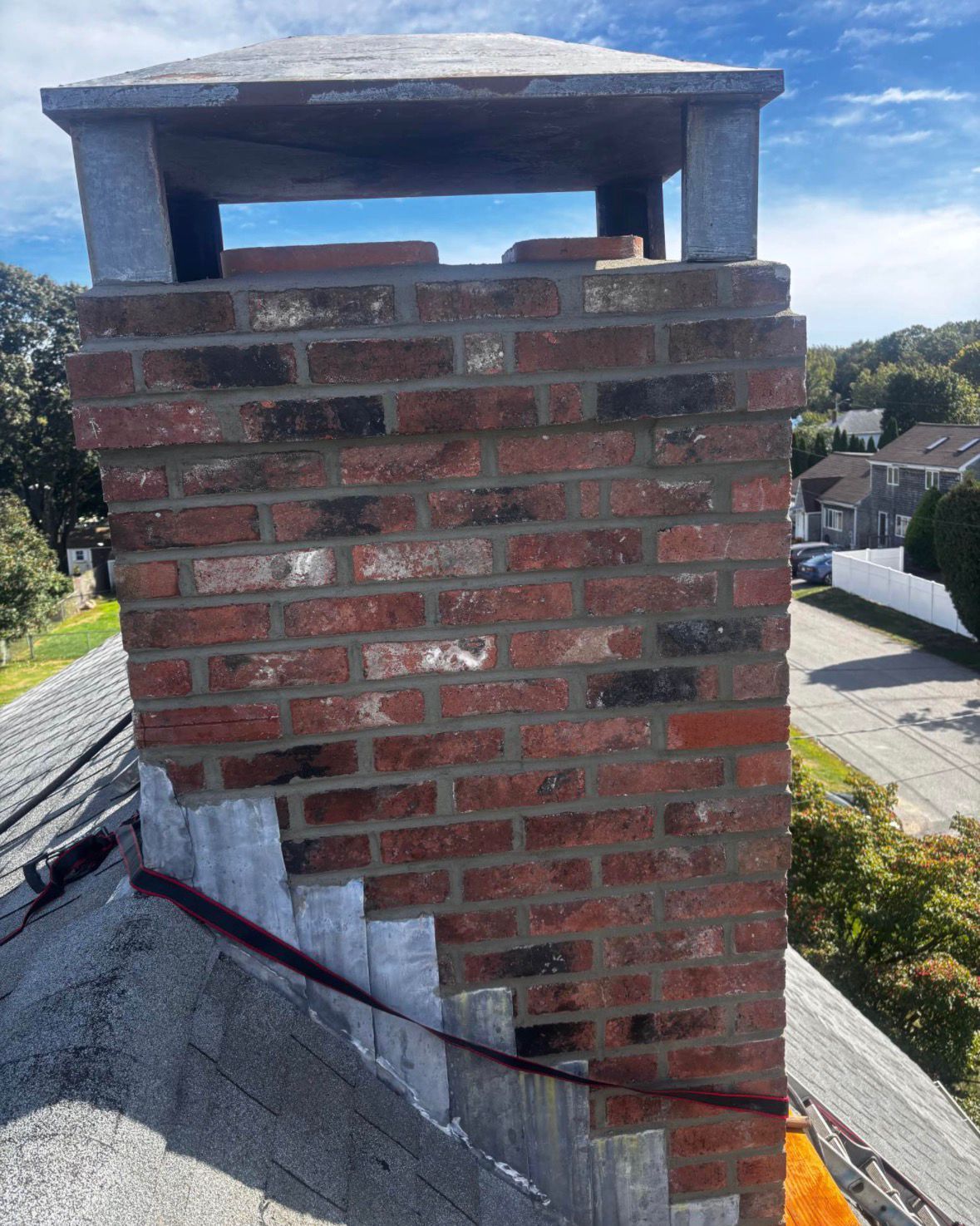 Brick chimney on a sloped shingle roof against a blue sky