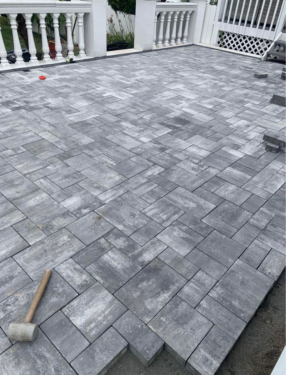 Gray paver patio with a rubber mallet on the left and white railing in the background