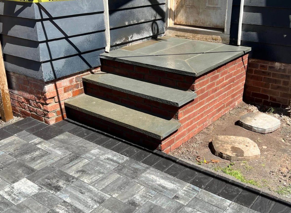 Outdoor brick steps with dark treads beside a gray paved walkway and a small garden bed