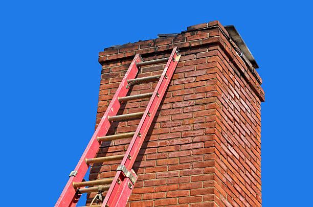 Red ladder leaning against a brick chimney against a blue sky