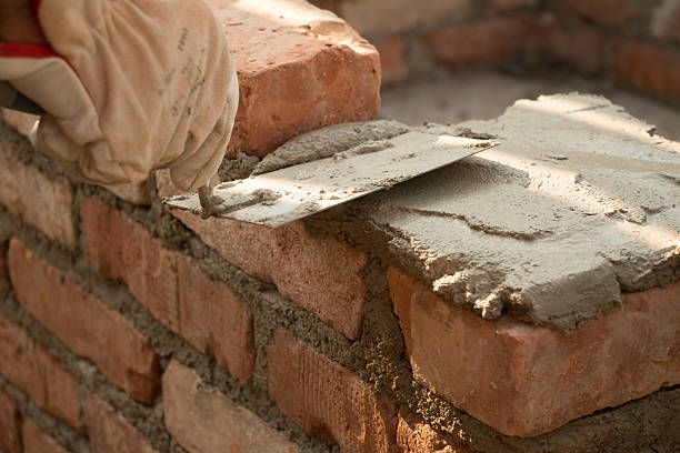 Bricklaying with a trowel spreading gray mortar on a brick wall