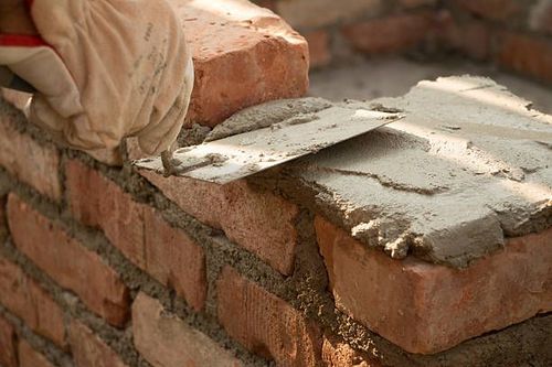 Gloved hands spreading mortar on a brick wall during masonry work