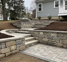 Stone patio with curved retaining walls and steps beside a gray house