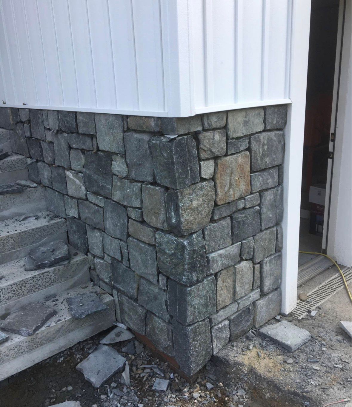 Stone retaining wall and stair corner beside a white building entrance with exposed ground below.