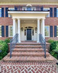 Brick colonial house entrance with white columns, black doors, and brick steps with iron railings
