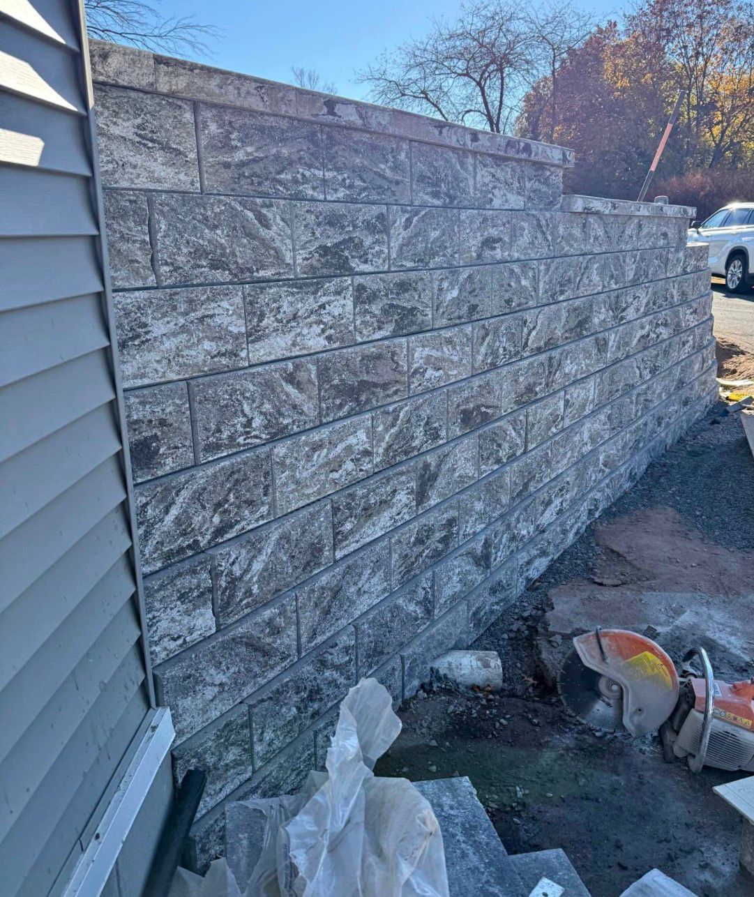 Stone retaining wall beside a house, with construction debris and a bucket on the ground.