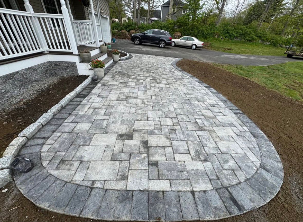 Curved stone-paver walkway beside a porch, bordered by mulch and gravel, leading toward a driveway.