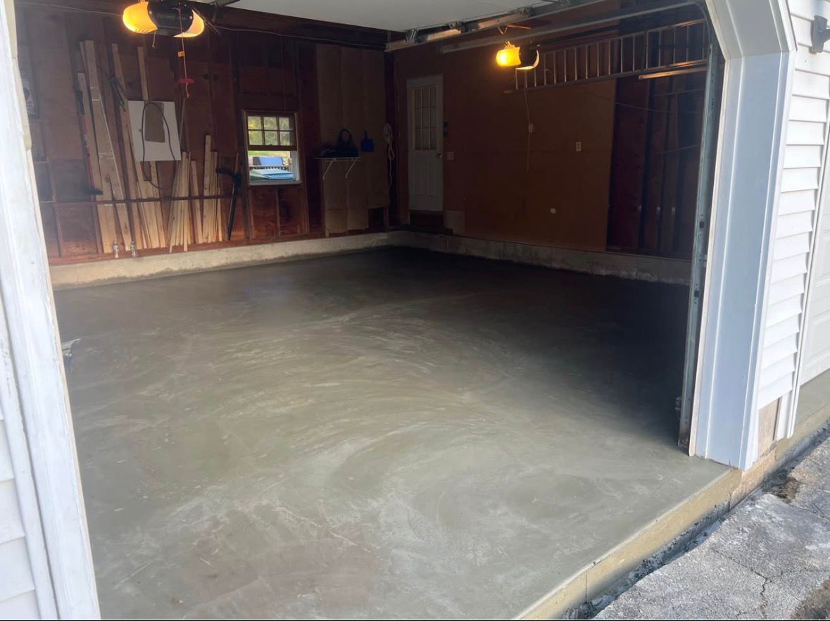 Empty garage with a concrete floor, wood-paneled walls, and a partially open white door.