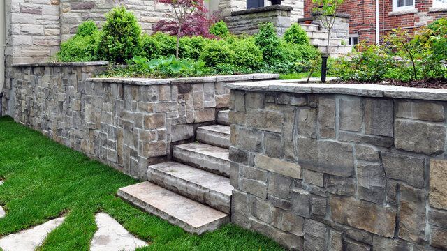 Stone retaining wall with steps leading up to a raised garden beside a grassy yard