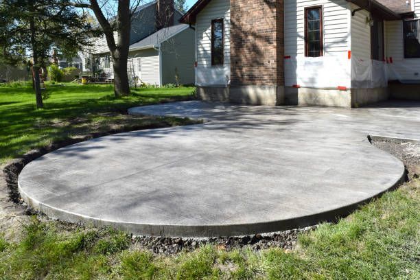 Fresh concrete patio slab beside a house, with lawn and trees in the background