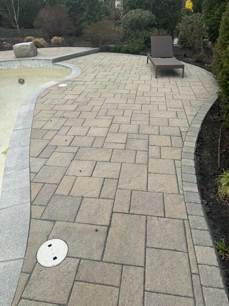 Stone-paver poolside walkway with a lounge chair and landscaped shrubs along the edge