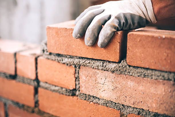 Gloved hand placing a red brick on a brick wall during construction