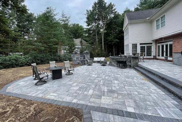 Stone patio with a fire pit, curved path, and lush garden trees under a bright blue sky