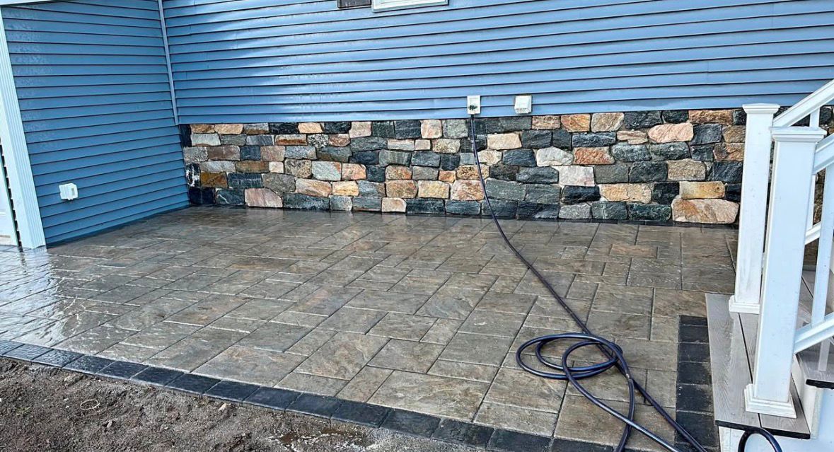 Stone patio against blue siding with a stacked-stone wall and white railing; coiled cable on the ground
