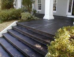 Dark front porch steps with a black deck, white columns, and surrounding shrubs