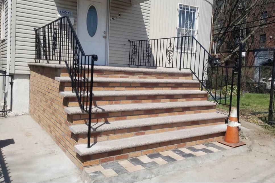 Brick front steps with black railings leading to a white house entrance, with an orange cone nearby.
