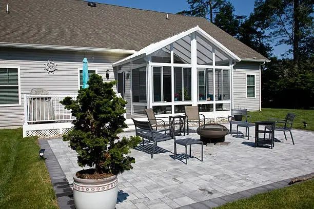 Patio with outdoor seating and fire pit beside a house with a white sunroom addition