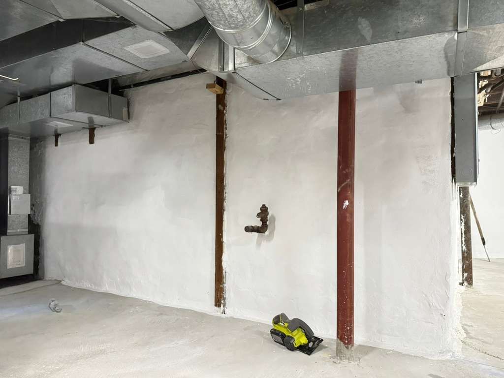 White basement wall under construction with exposed ductwork, red support columns, and a yellow tool on the floor