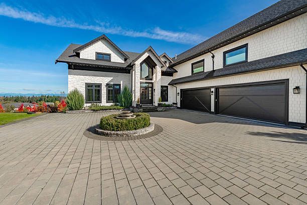 Modern two-story suburban house with a large paved driveway and attached garage under a blue sky