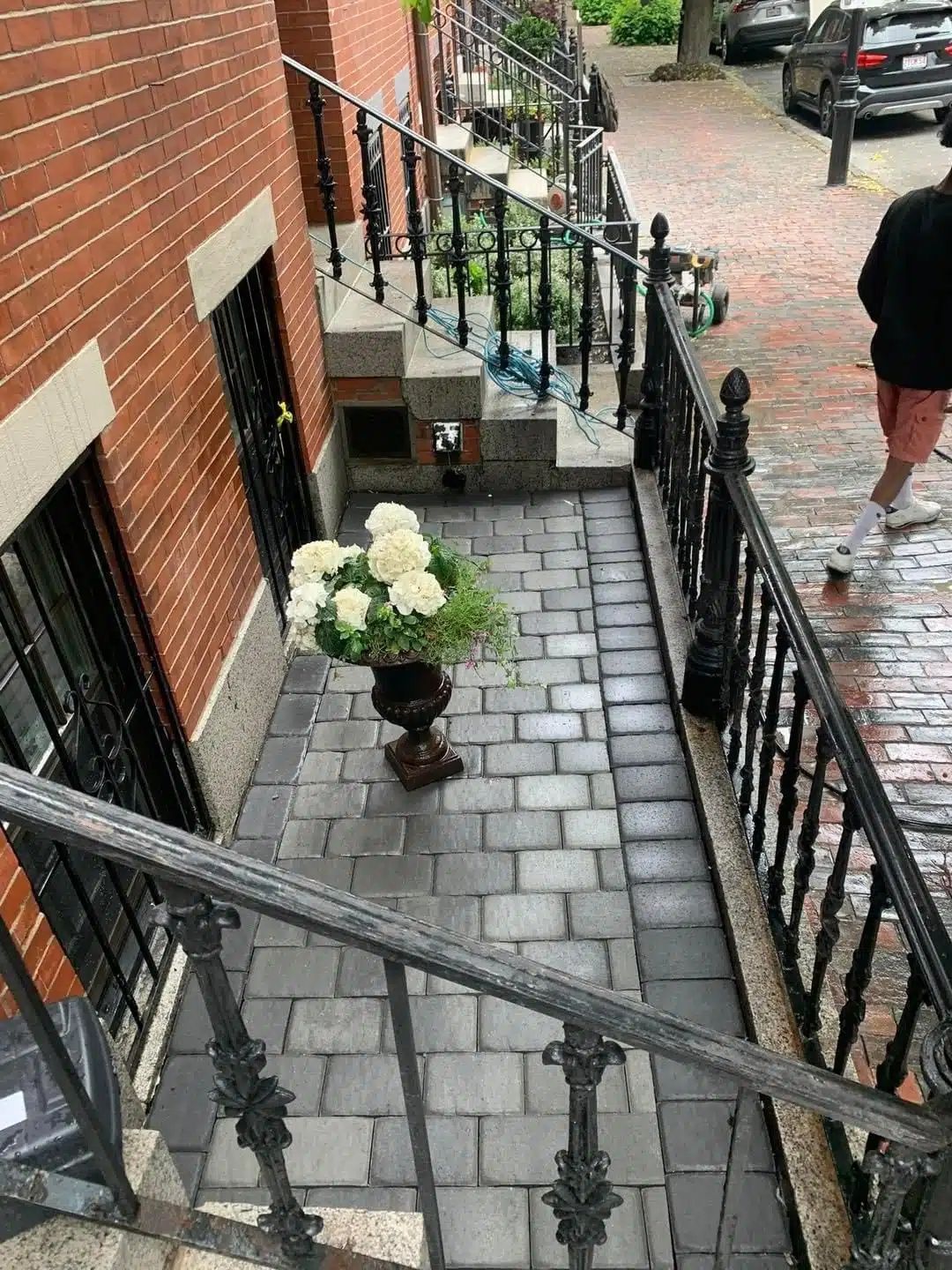 Brick stoop with black railings, potted white flowers, and a person standing on the sidewalk nearby