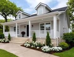 White house with front porch, dormer windows, and landscaped flower beds beside a driveway